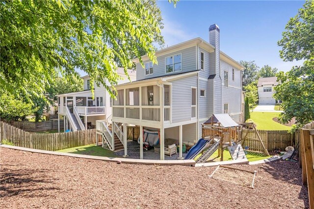 rear view of house featuring a sunroom, stairway, a fenced backyard, a chimney, and a playground