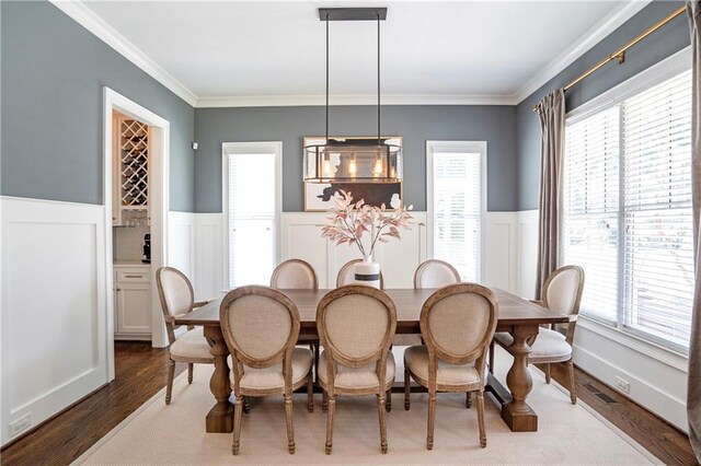 dining room featuring crown molding, wood finished floors, a healthy amount of sunlight, and a wainscoted wall