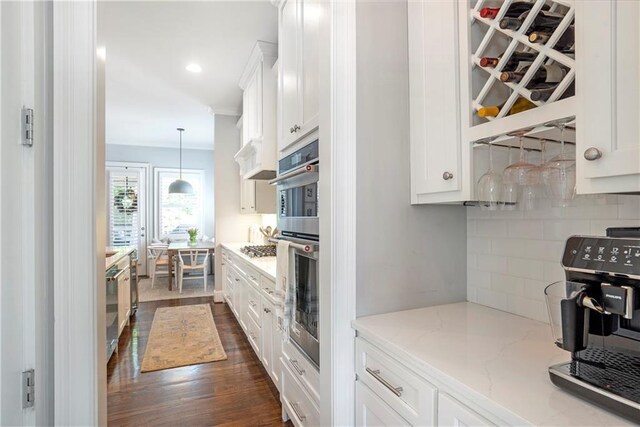 kitchen with decorative backsplash, appliances with stainless steel finishes, light stone countertops, white cabinets, and dark wood-type flooring