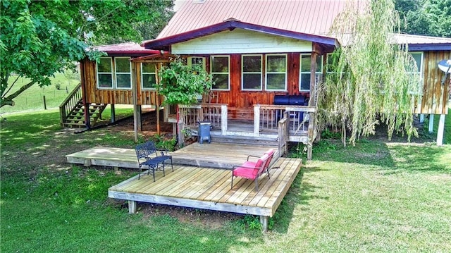 back of house featuring a sunroom, metal roof, a wooden deck, and a lawn