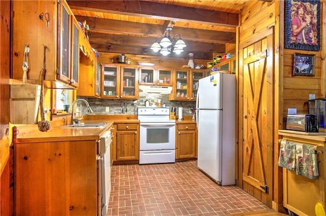 kitchen with white appliances, wooden walls, brown cabinetry, an inviting chandelier, and under cabinet range hood