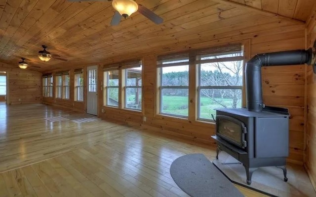 unfurnished living room featuring ceiling fan, light wood-type flooring, a wood stove, wood walls, and wooden ceiling