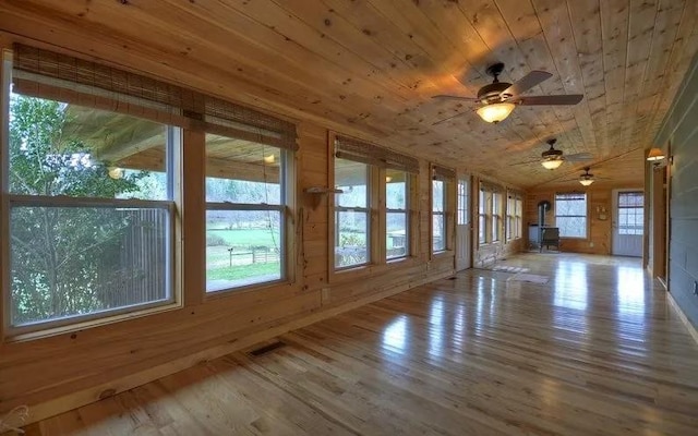 unfurnished sunroom with wood ceiling, ceiling fan, vaulted ceiling, and a wood stove