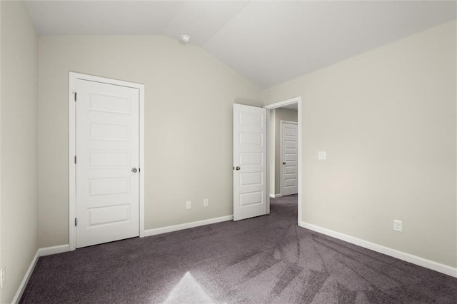 unfurnished bedroom with lofted ceiling, dark colored carpet, and baseboards