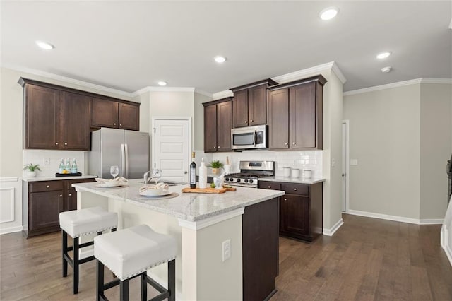 kitchen featuring dark brown cabinetry, an island with sink, appliances with stainless steel finishes, a breakfast bar, and light stone countertops