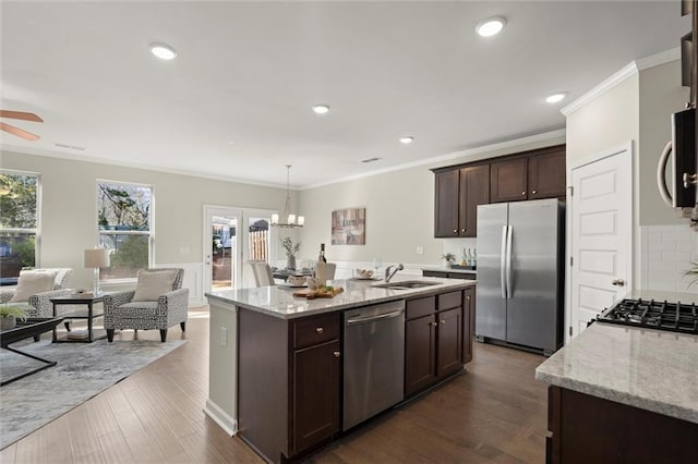 kitchen featuring decorative light fixtures, stainless steel appliances, a kitchen island with sink, a sink, and light stone countertops