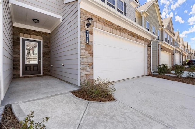 view of exterior entry with a garage, a residential view, stone siding, and driveway