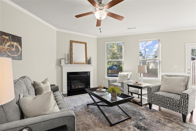 living room featuring ornamental molding, visible vents, a fireplace with flush hearth, and a ceiling fan