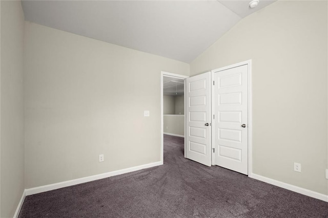 unfurnished bedroom with lofted ceiling, dark carpet, and baseboards