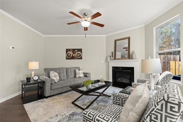 living room featuring baseboards, ornamental molding, wood finished floors, and a glass covered fireplace