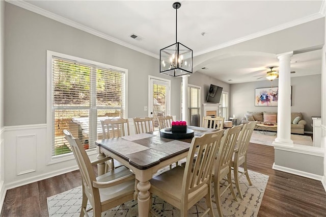 dining space featuring visible vents, a ceiling fan, dark wood-style floors, a fireplace, and decorative columns