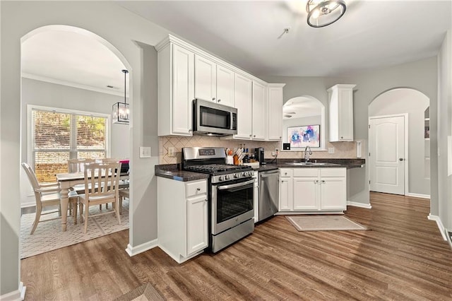 kitchen featuring dark countertops, dark wood finished floors, arched walkways, stainless steel appliances, and a sink