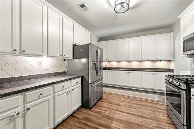 kitchen featuring wood finished floors, visible vents, stainless steel appliances, white cabinets, and tasteful backsplash