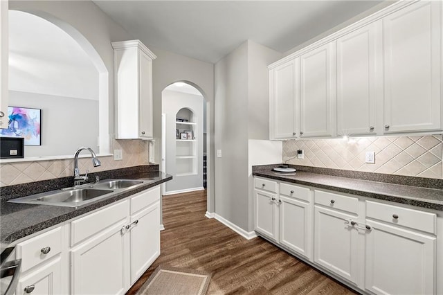 kitchen featuring dark countertops, a sink, baseboards, white cabinetry, and dark wood-style flooring