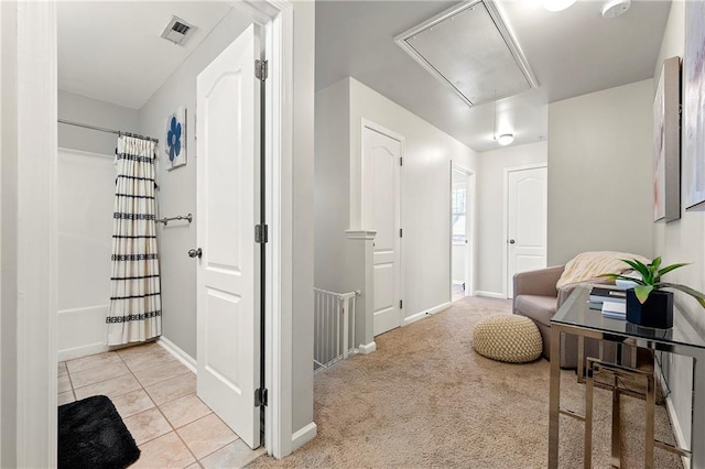 corridor featuring visible vents, light carpet, light tile patterned floors, baseboards, and attic access