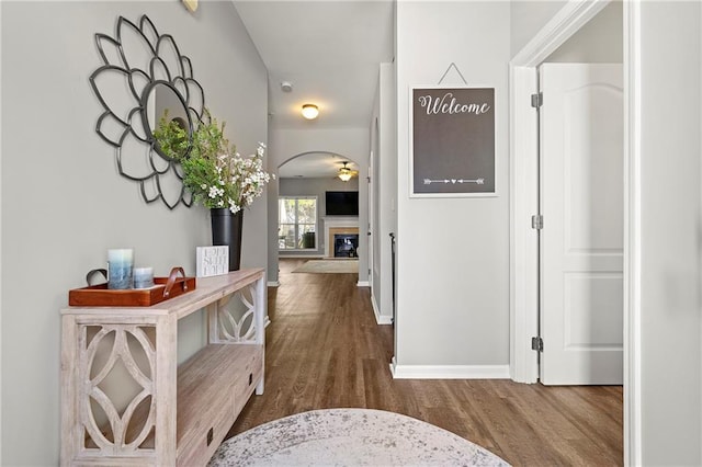 corridor featuring wood finished floors, arched walkways, and baseboards