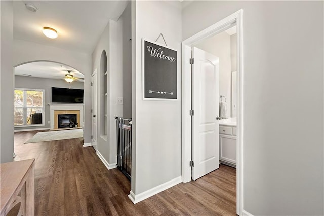 hallway with dark wood-style floors, arched walkways, and baseboards