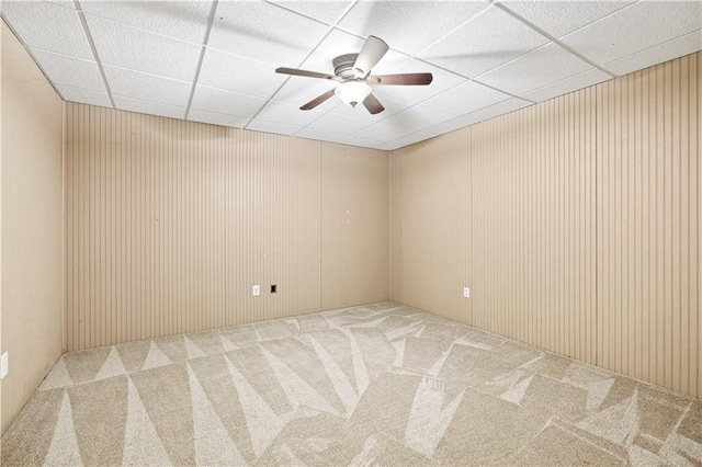 carpeted spare room with a paneled ceiling, wood walls, and ceiling fan