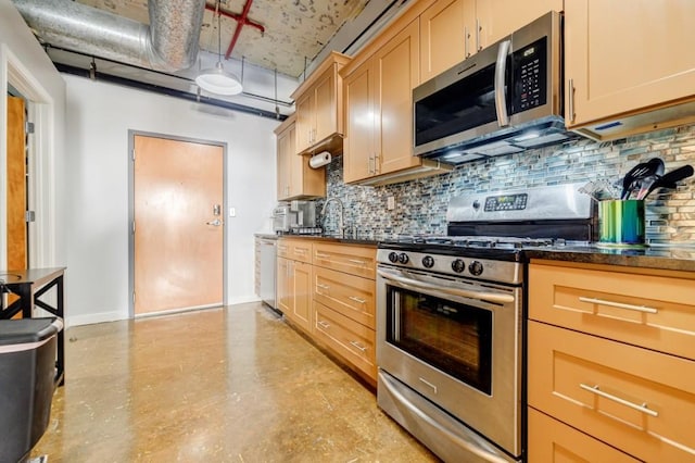 kitchen featuring dark countertops, backsplash, appliances with stainless steel finishes, a sink, and baseboards