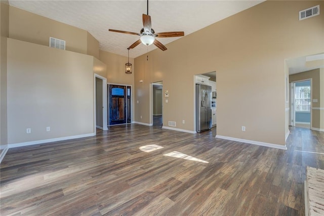 unfurnished living room with a towering ceiling, a textured ceiling, dark hardwood / wood-style floors, and ceiling fan