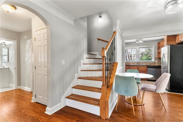 staircase featuring hardwood / wood-style flooring, an inviting chandelier, ornamental molding, and sink