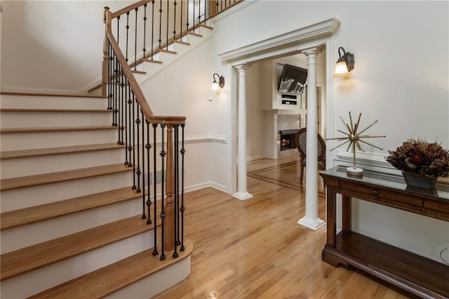 135 Stone Orchard Ct, Milton, GA 30004 - staircase featuring decorative columns, wood finished floors, a lit fireplace, and baseboards