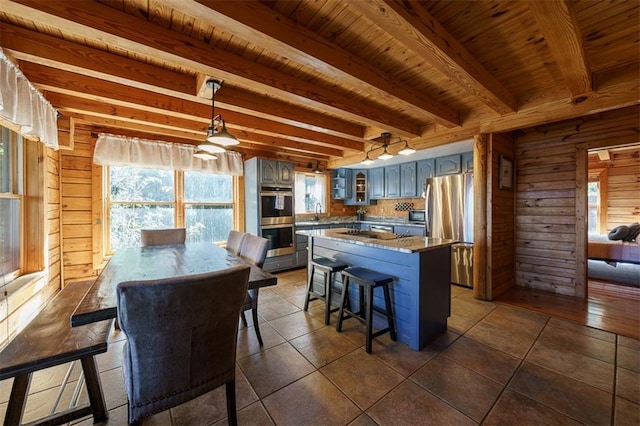 tiled dining space with wood ceiling, beam ceiling, sink, and wood walls
