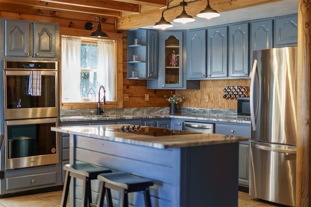 kitchen featuring pendant lighting, sink, appliances with stainless steel finishes, wooden walls, and a center island