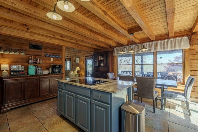 kitchen featuring light stone counters, hanging light fixtures, a kitchen island, beamed ceiling, and black electric stovetop