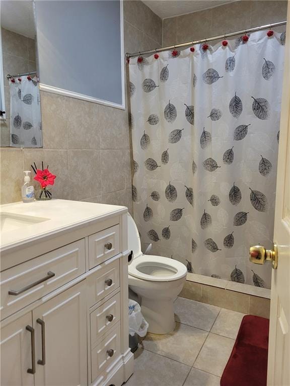 full bathroom with a tile shower, tile patterned floors, tile walls, toilet, and vanity