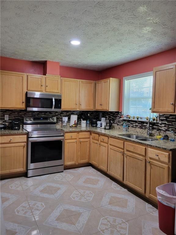 kitchen with stone counters, a sink, backsplash, and stainless steel appliances