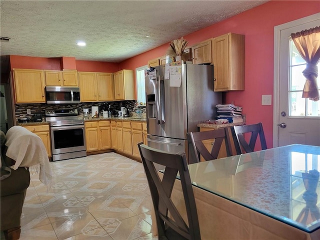 kitchen featuring recessed lighting, stainless steel appliances, light brown cabinetry, backsplash, and a textured ceiling
