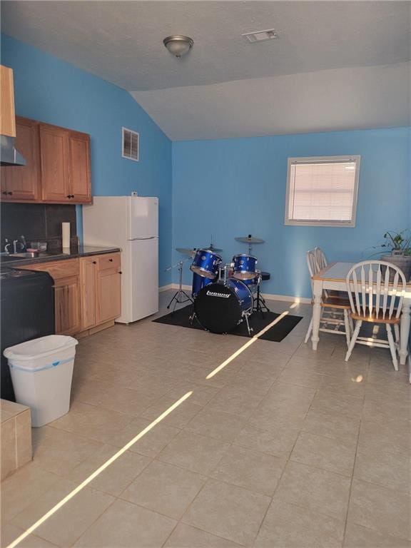 kitchen with ventilation hood, visible vents, light tile patterned flooring, and vaulted ceiling