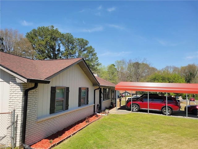 view of side of home with brick siding, a detached carport, a yard, and roof with shingles