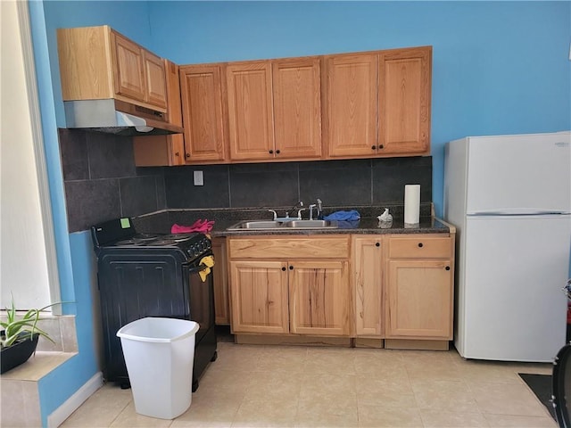 kitchen featuring a sink, under cabinet range hood, range, dark countertops, and freestanding refrigerator