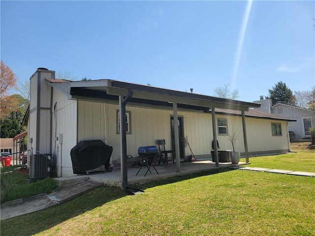 rear view of property featuring a lawn, a chimney, central air condition unit, and a patio