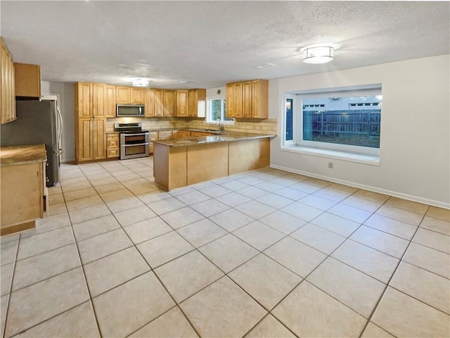 kitchen with kitchen peninsula, light tile patterned flooring, a textured ceiling, and appliances with stainless steel finishes