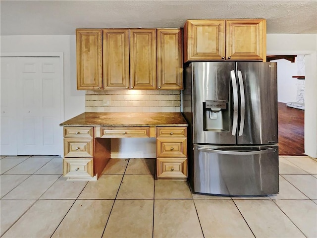 kitchen with stainless steel refrigerator with ice dispenser, light stone countertops, light tile patterned flooring, a textured ceiling, and decorative backsplash