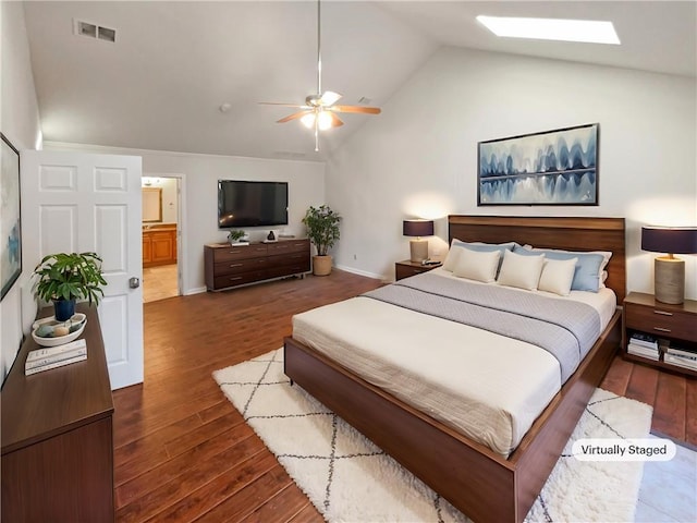 bedroom featuring ceiling fan, hardwood / wood-style floors, vaulted ceiling with skylight, and ensuite bath