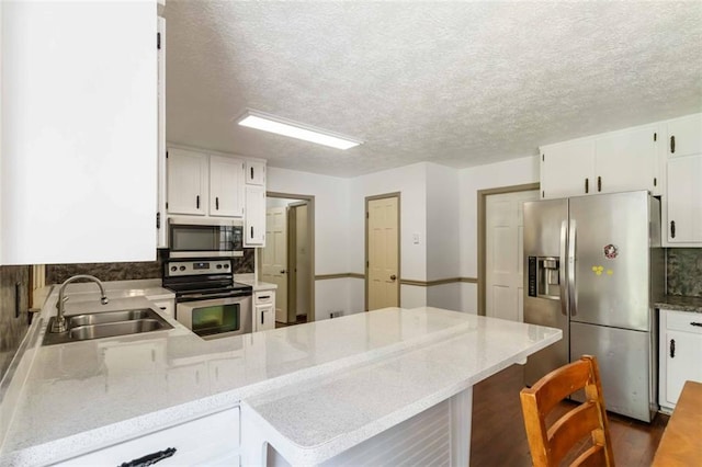 kitchen with a sink, white cabinets, appliances with stainless steel finishes, and a peninsula