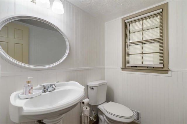 half bathroom featuring a textured ceiling, visible vents, wainscoting, a sink, and toilet