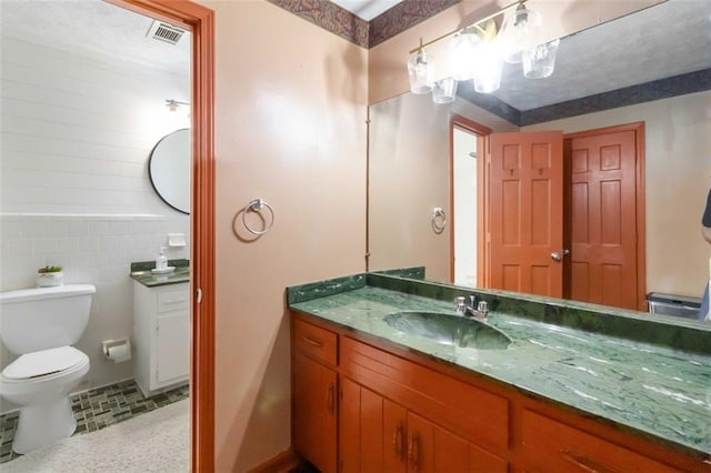 bathroom with vanity, toilet, tile walls, and visible vents