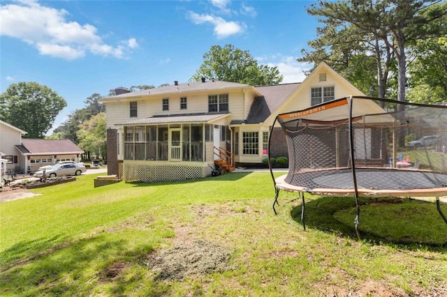 back of house with a sunroom, a trampoline, and a lawn