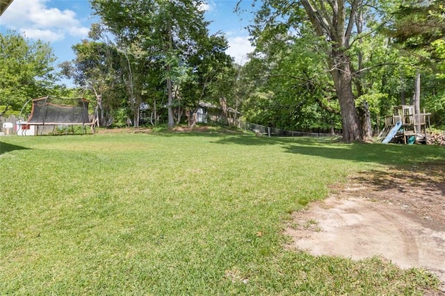 view of yard with a playground, fence, and a trampoline