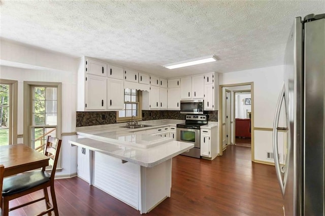 kitchen featuring dark wood-style flooring, a peninsula, light countertops, white cabinets, and appliances with stainless steel finishes