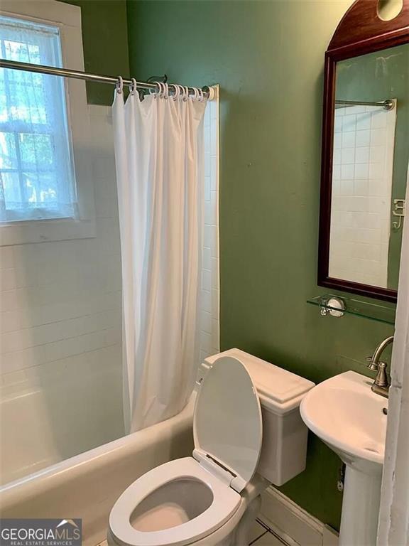 bathroom featuring toilet, shower / bath combo, and a sink