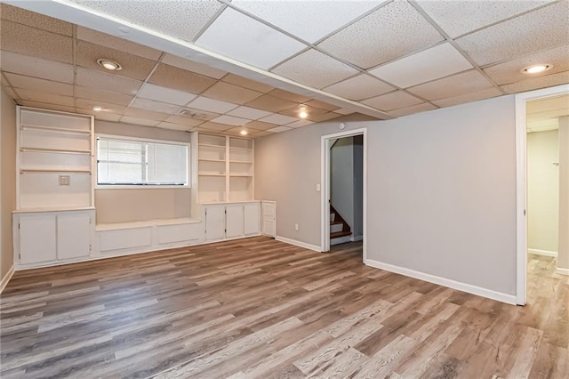 interior space with built in shelves, a drop ceiling, and hardwood / wood-style flooring