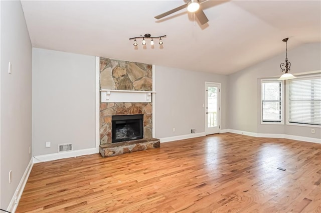 unfurnished living room with light wood-type flooring, rail lighting, vaulted ceiling, ceiling fan, and a stone fireplace