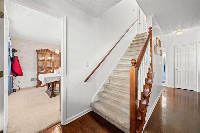 staircase featuring visible vents, a wainscoted wall, a textured ceiling, and wallpapered walls