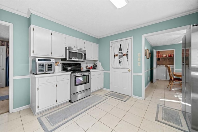 kitchen featuring stainless steel appliances, washer and dryer, light tile patterned flooring, and white cabinetry